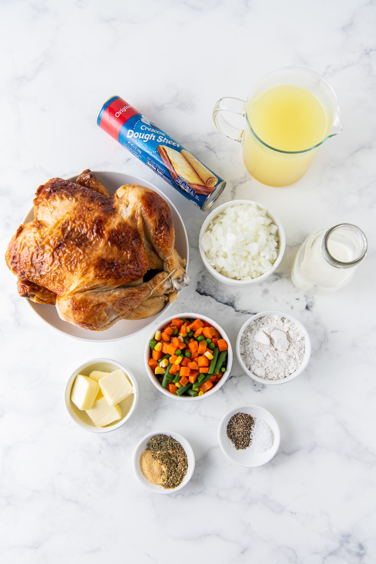 ingredients to make chicken pot pie casserole including a whole chicken, vegetables, butter, seasonings, and crescent rolls