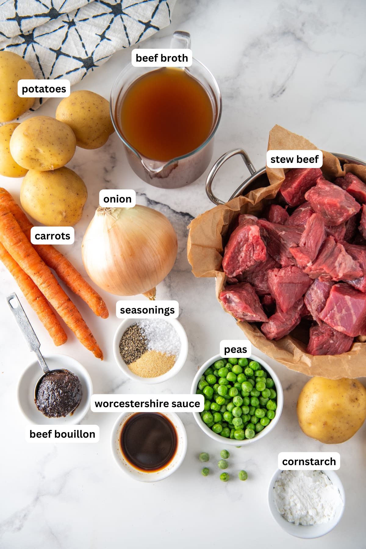 The ingredients for crockpot beef stew recipe in order from top to bottom: potatoes, beef broth, carrots, onion, stew beef, seasonings, beef bouillon, worcestershire, peas, cornstarch.