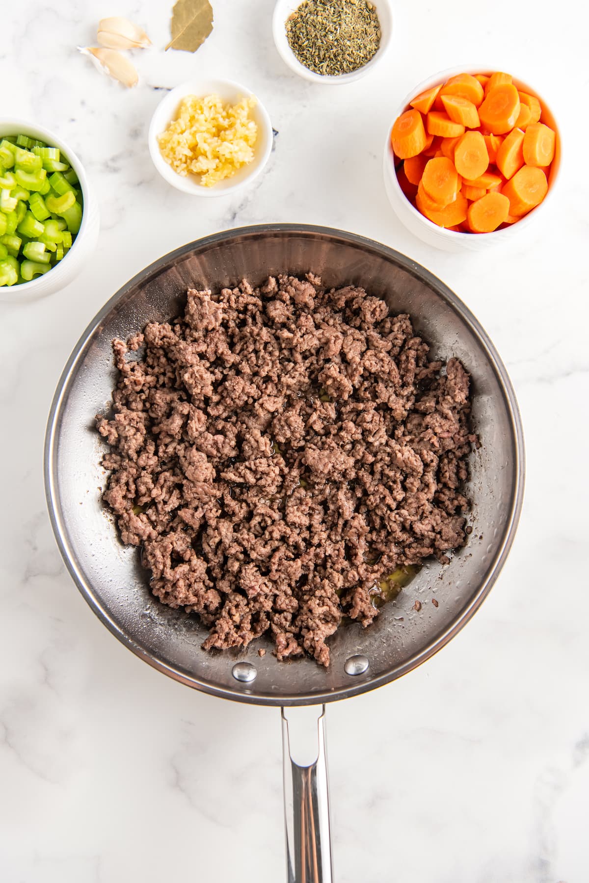 a bowl of ground beef next to small bowls of chopped vegetables