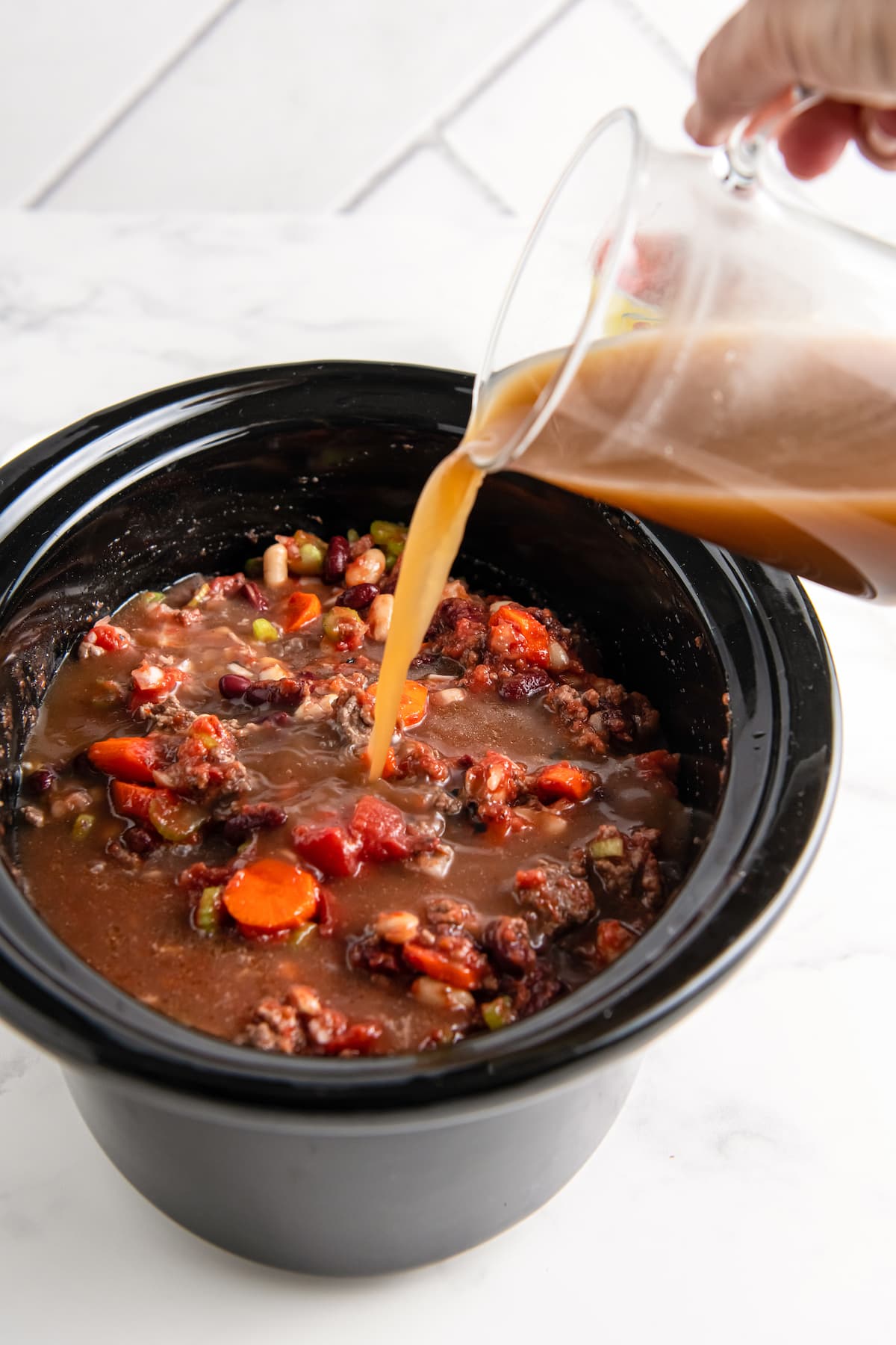 pouring beef broth into a crockpot with other soup ingredients
