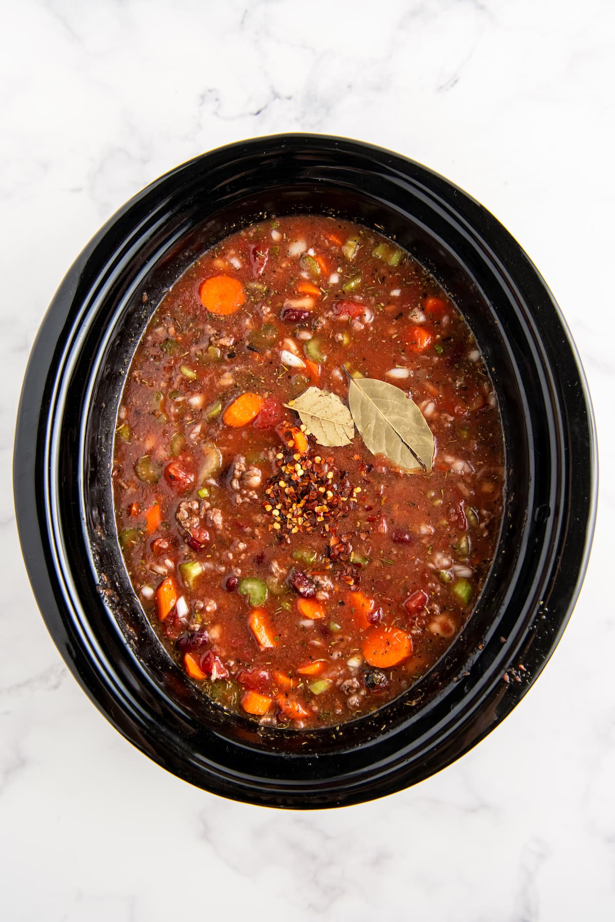 a rich tomato based broth with vegetables, beans, and bay leaf in a crockpot