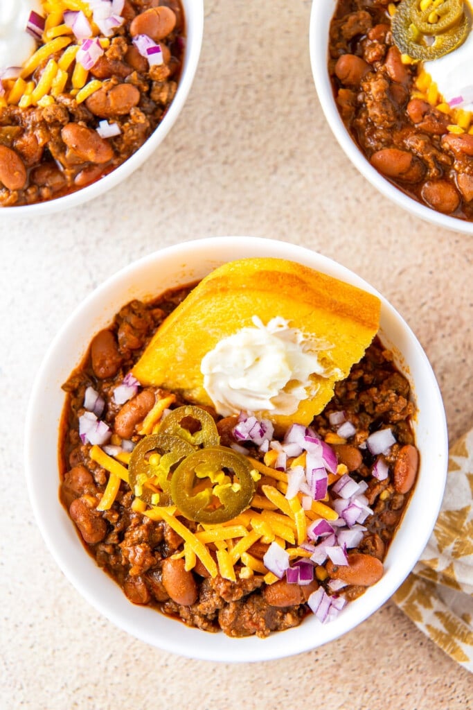 A bowl of stovetop beef chili topped with buttered cornbread. 