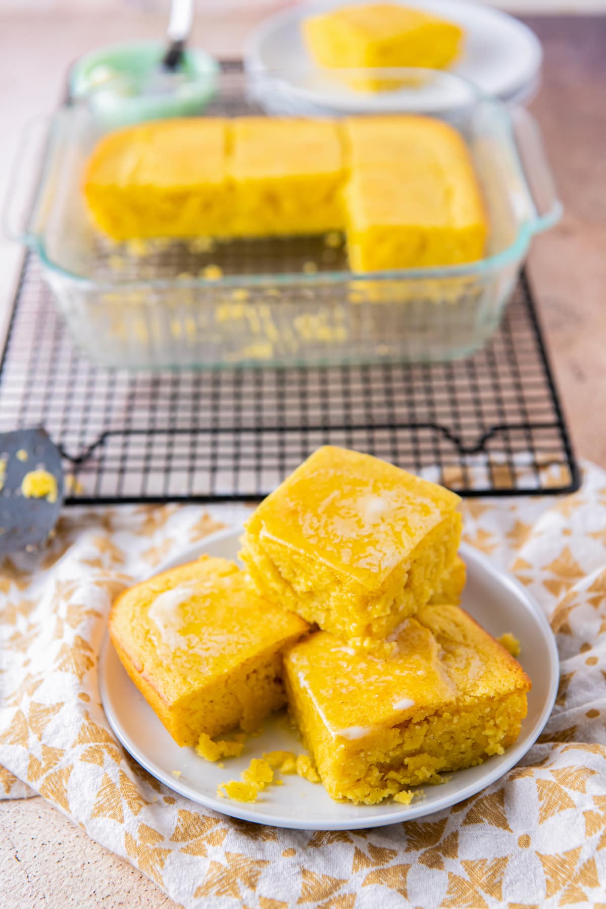 a plate of cornbread pieces next to a cooling rack with a pan on it