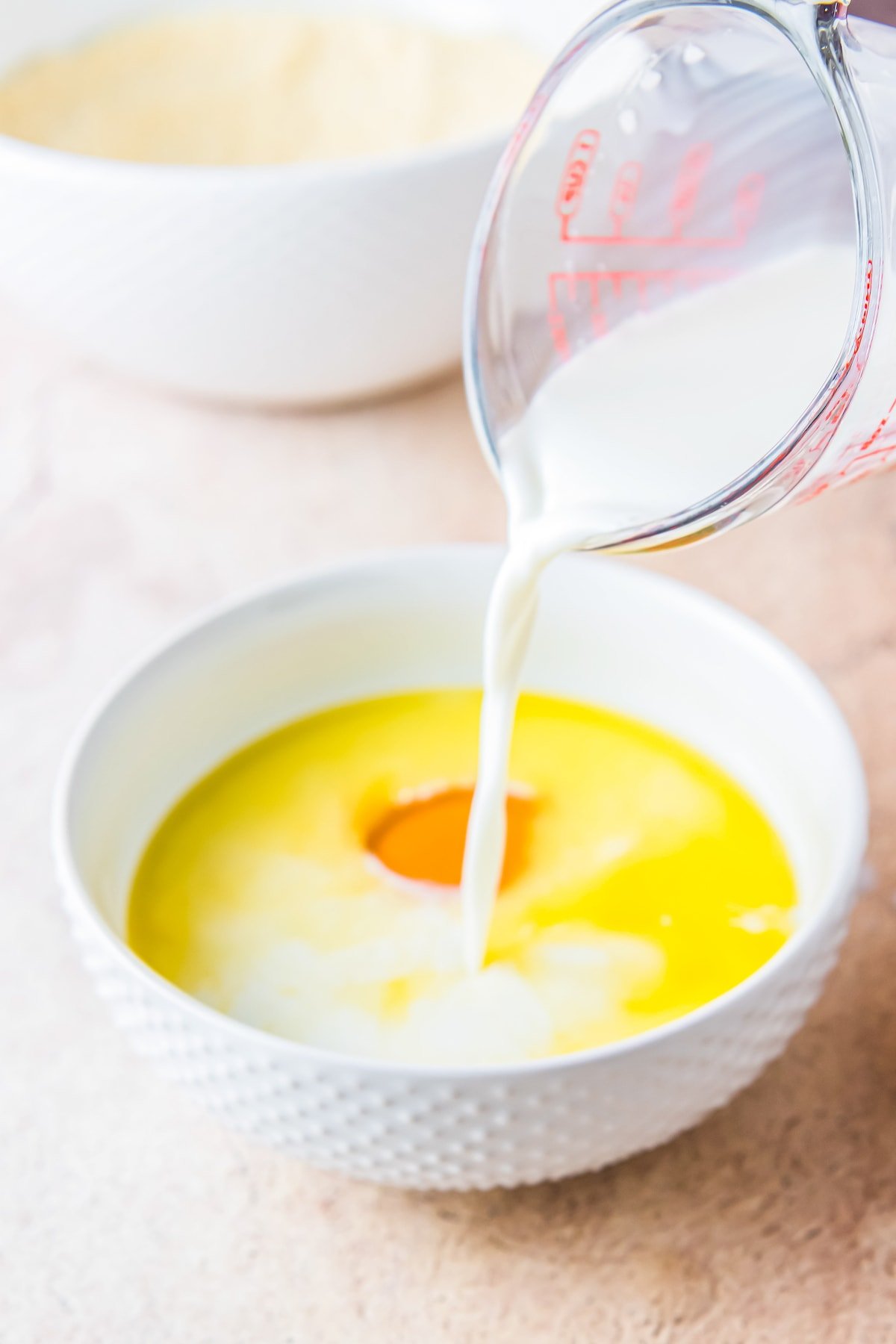 pouring milk into a mixing bowl with egg and melted butter