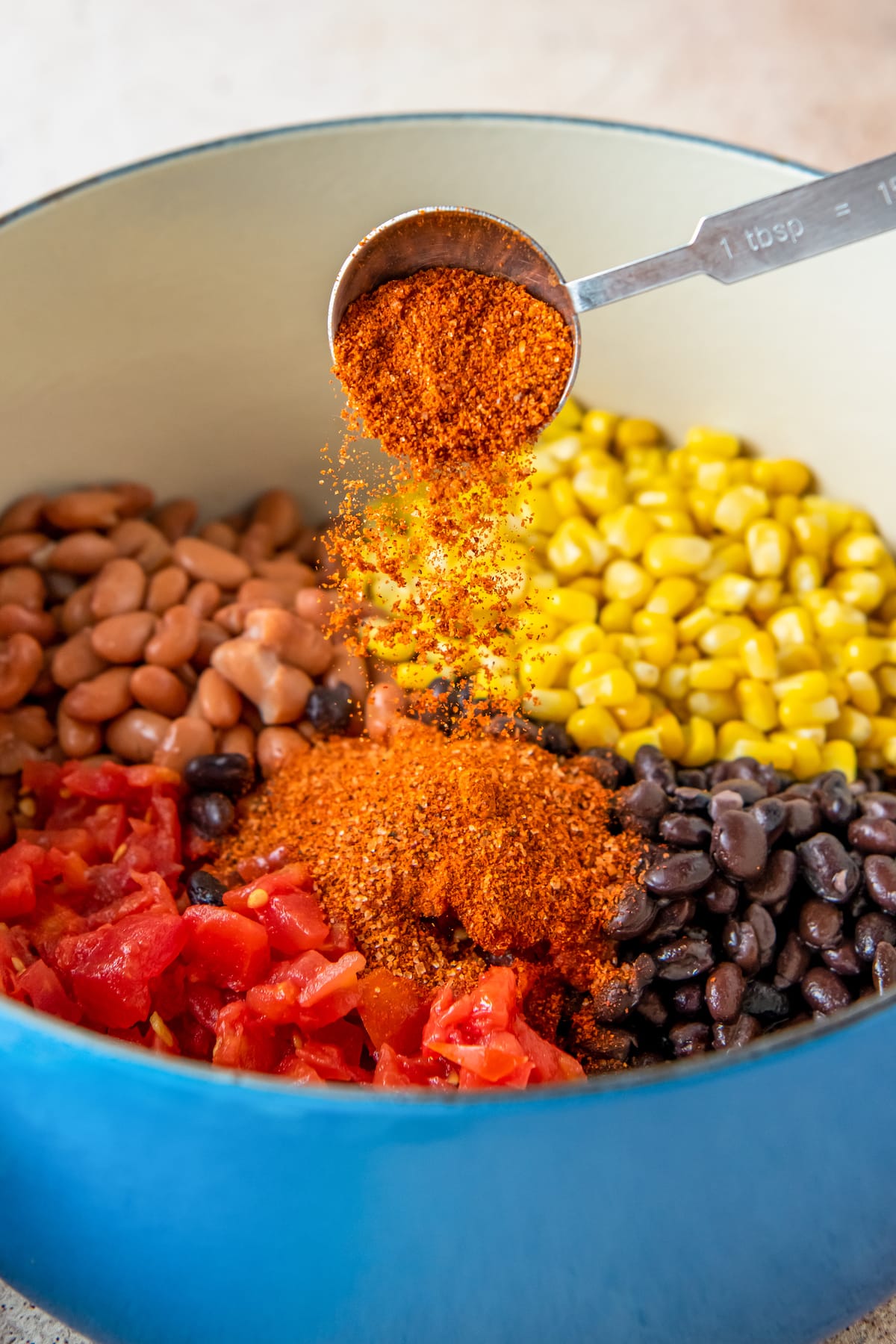 seasoning tomatoes, beans, and corn in a soup pot