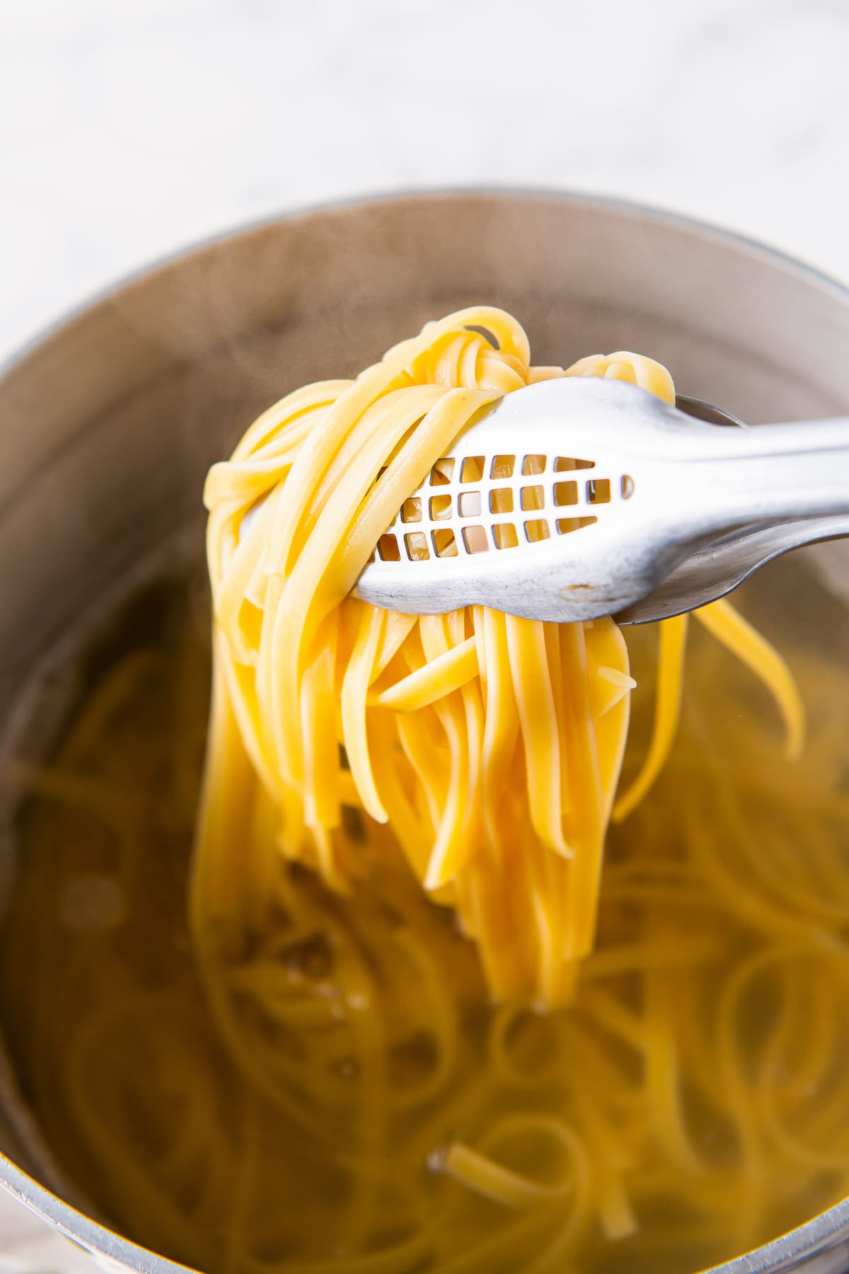 scooping noodles with tongs in a pot