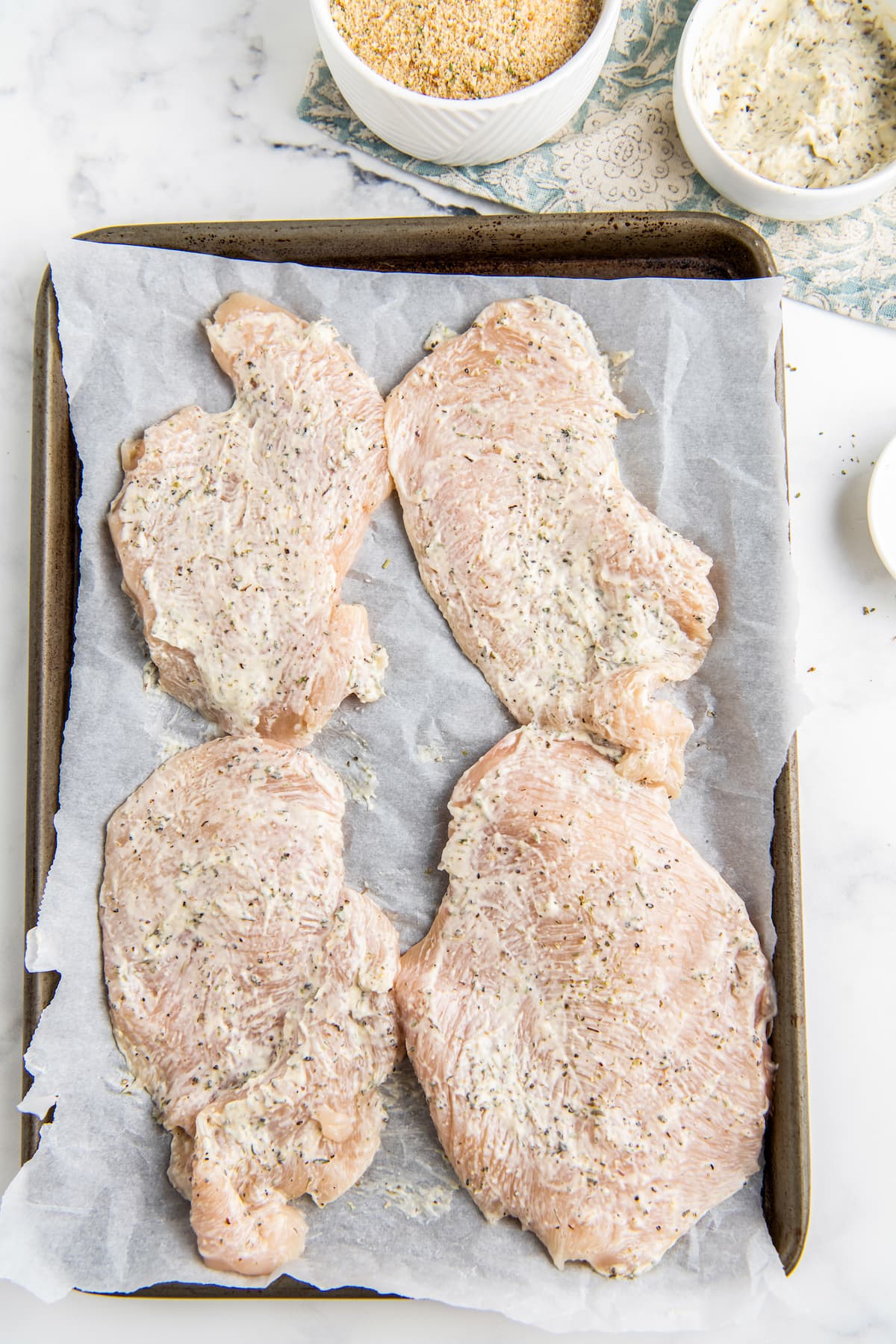 four chicken breasts brushed with mayo on a sheet tray