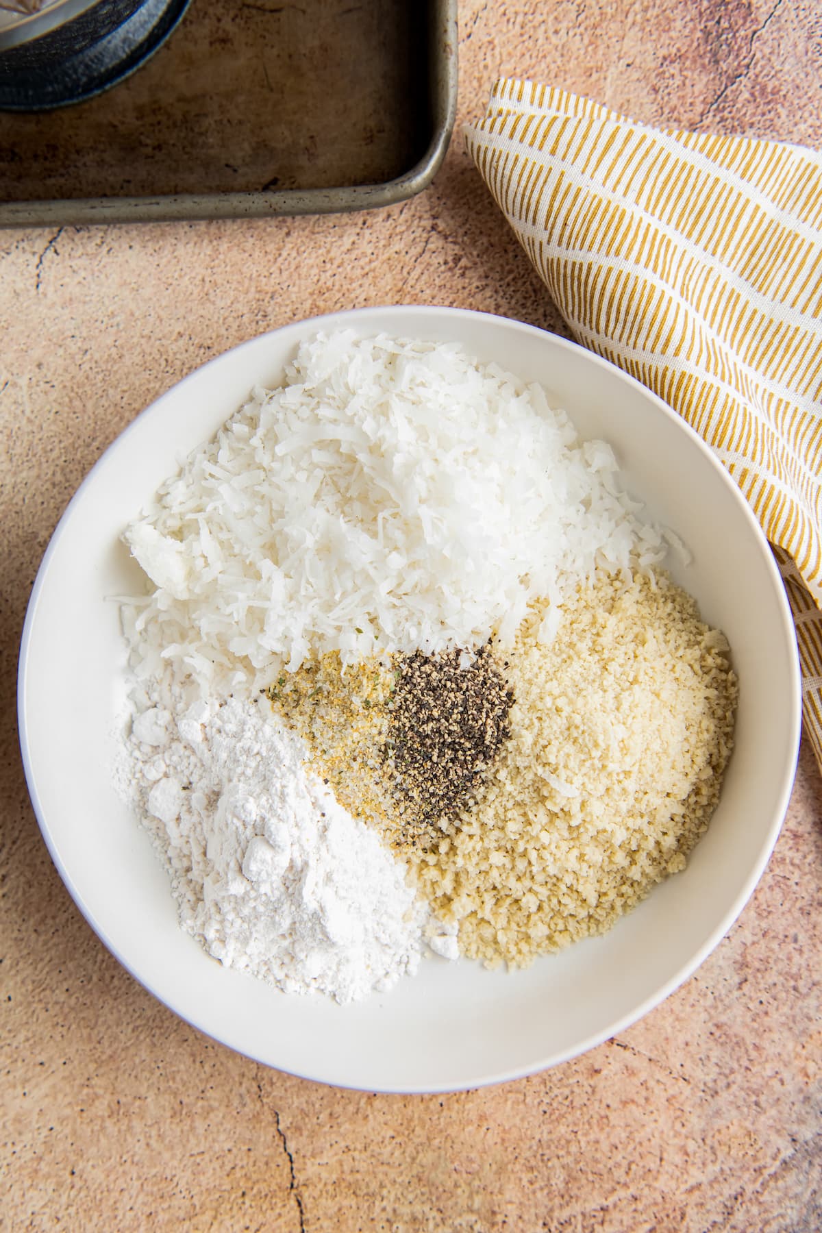 a bowl with dry ingredients like flour, coconut flakes, and seasonings