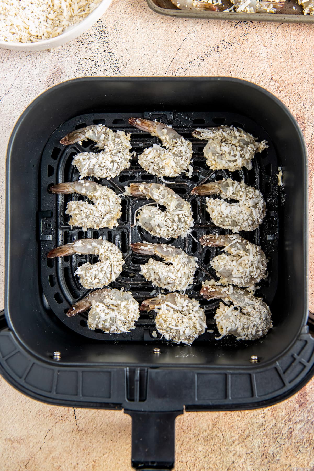 shrimp that have been dredged in flour and coconut in an air fryer tray