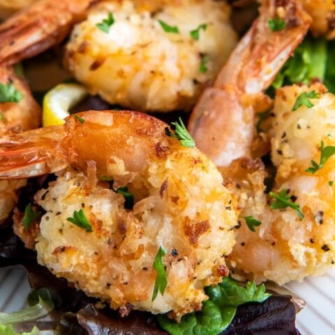a close up of air fryer coconut shrimp with a golden brown crust and herb garnish