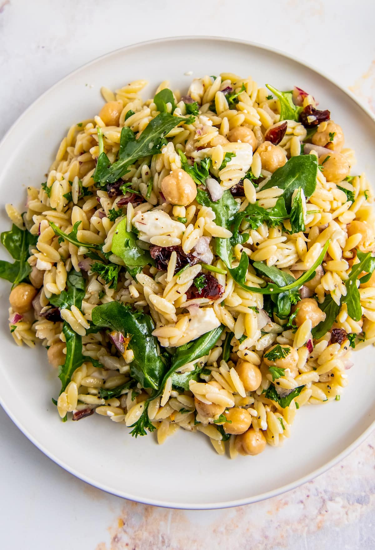 a plate of a salad made with orzo, arugula, red onion, garbanzo beans, and feta