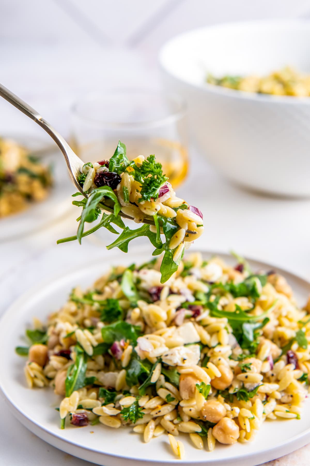 a fork taking a bite of Orzo Salad with Arugula, red onions, feta, and herbs