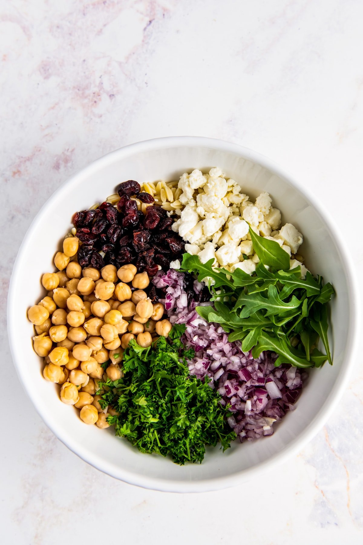 an assortment of chickpeas, arugula, feta, dried cranberries, and red onion in a large bowl