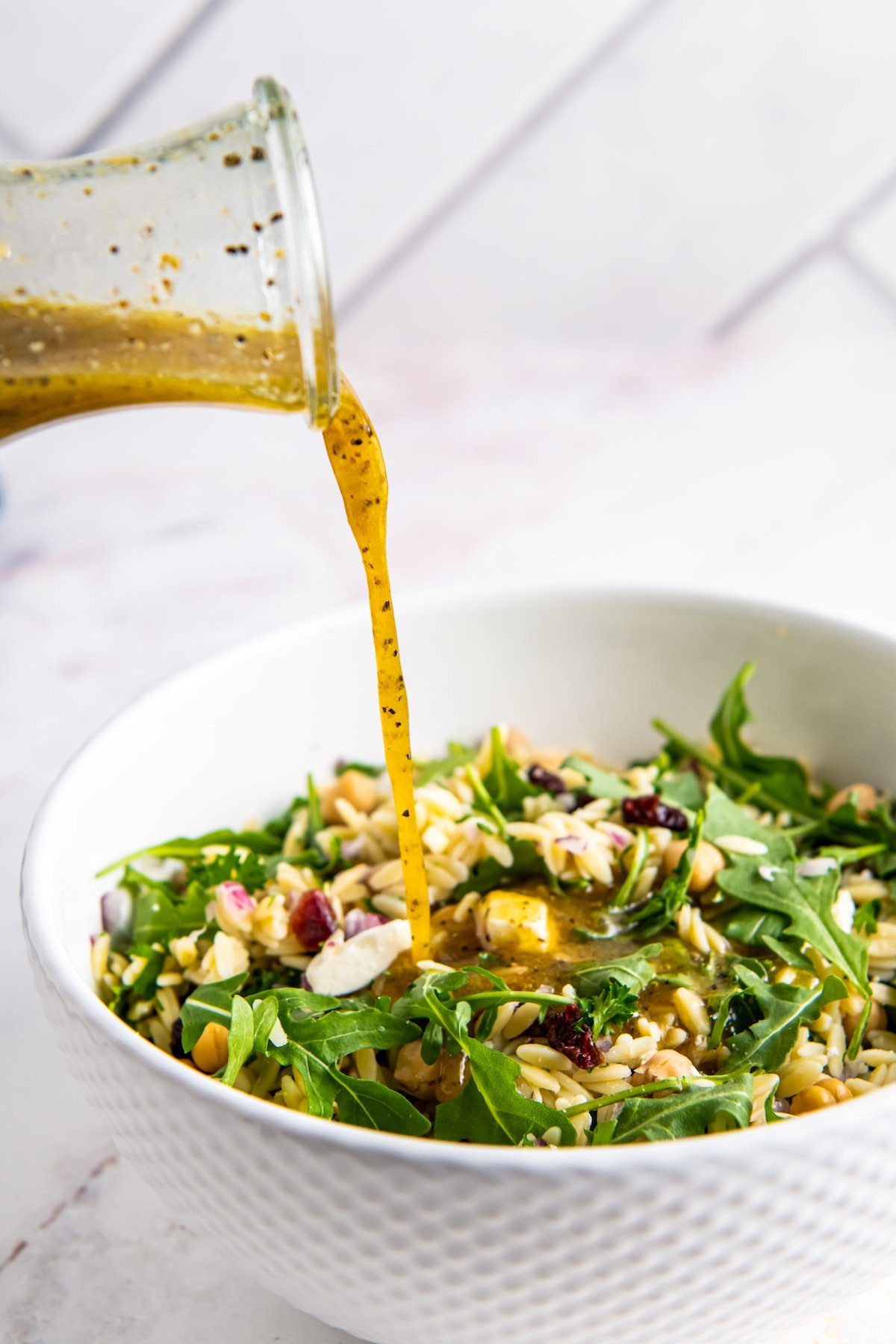 pouring dressing over a salad with arugula and orzo