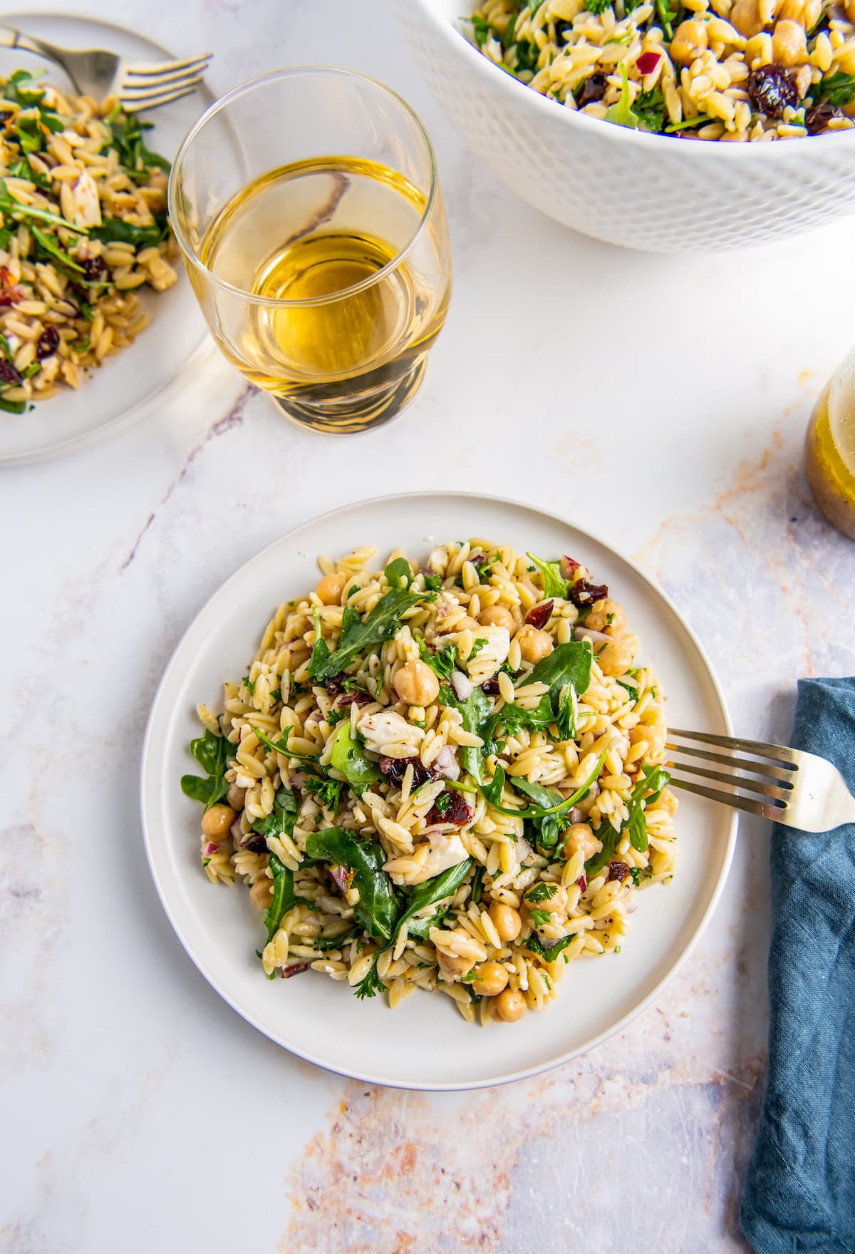 a plate of a salad made with orzo, arugula, red onion, garbanzo beans, and feta next to a glass of white wine