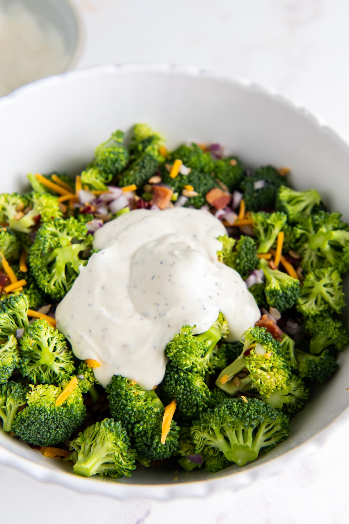 broccoli in a bowl with other salad ingredients with a scoop of creamy dressing on top