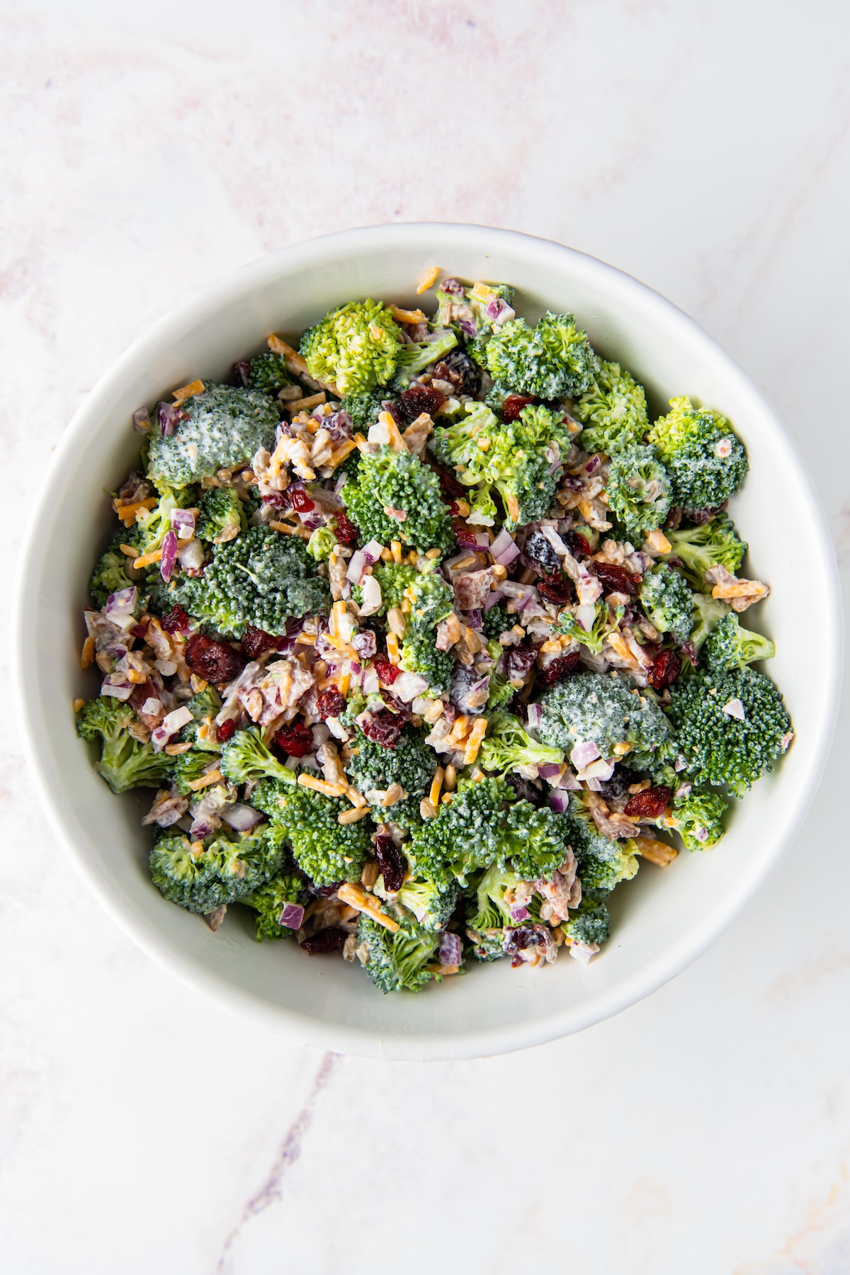 a bowl of broccoli salad with red onions, bacon, and shredded cheese