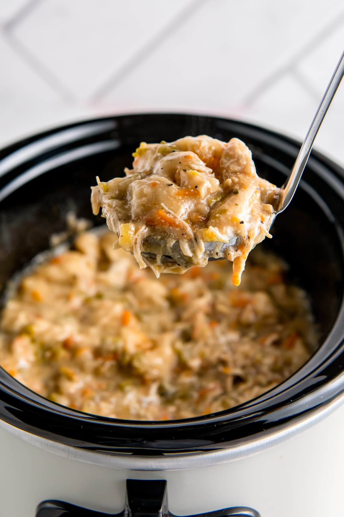 a ladle of chicken and dumplings over a crockpot