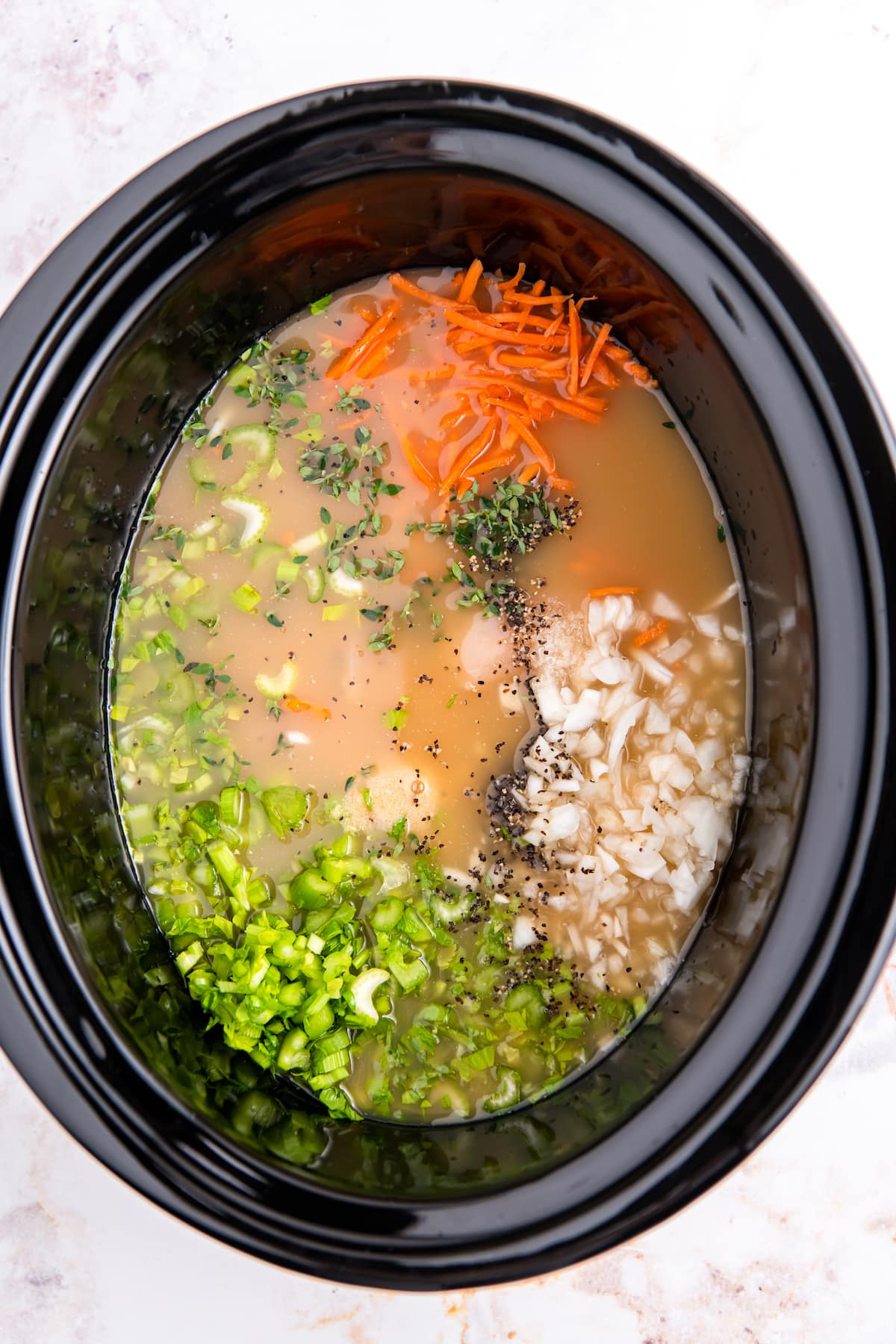 broth in a crockpot filled with diced celery, carrots, onions, and seasonings