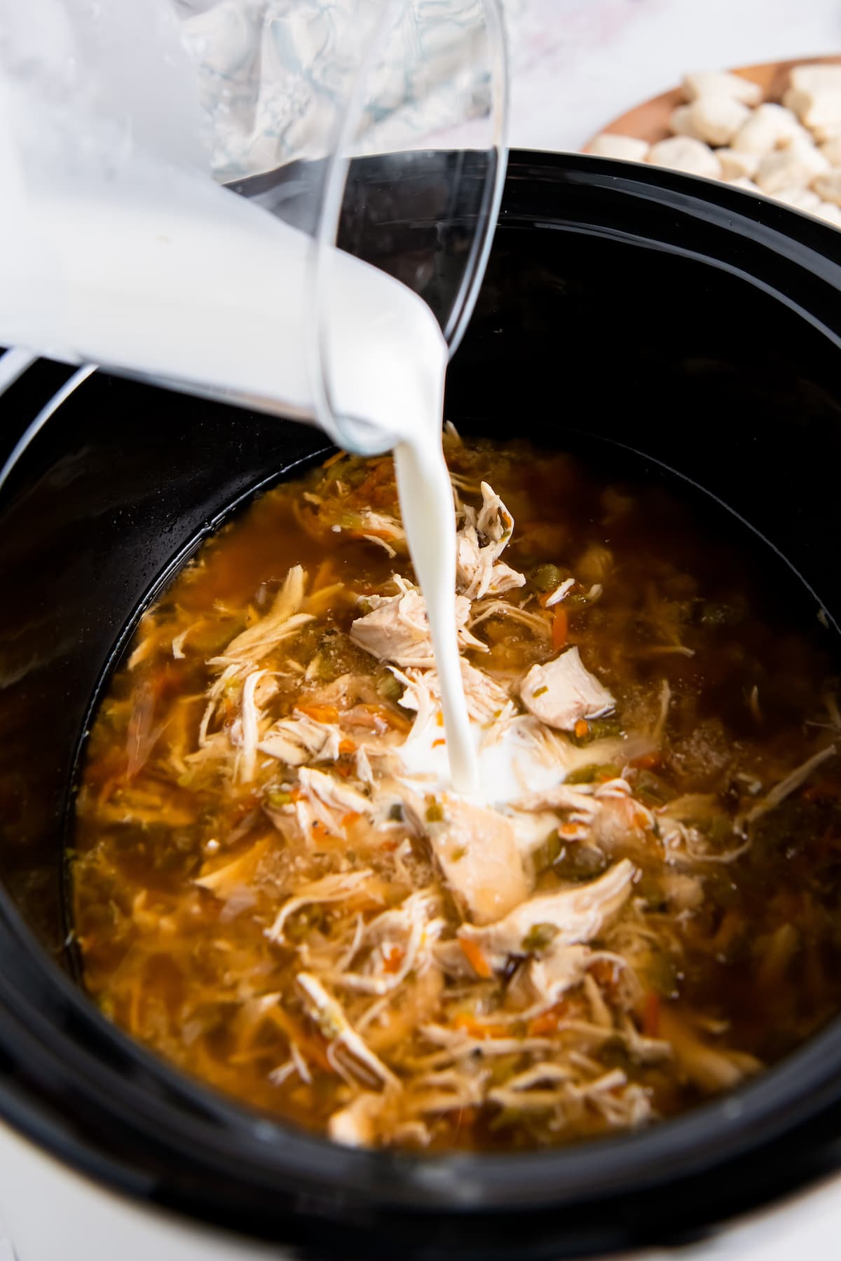 pouring cream into a crockpot with shredded chicken and broth