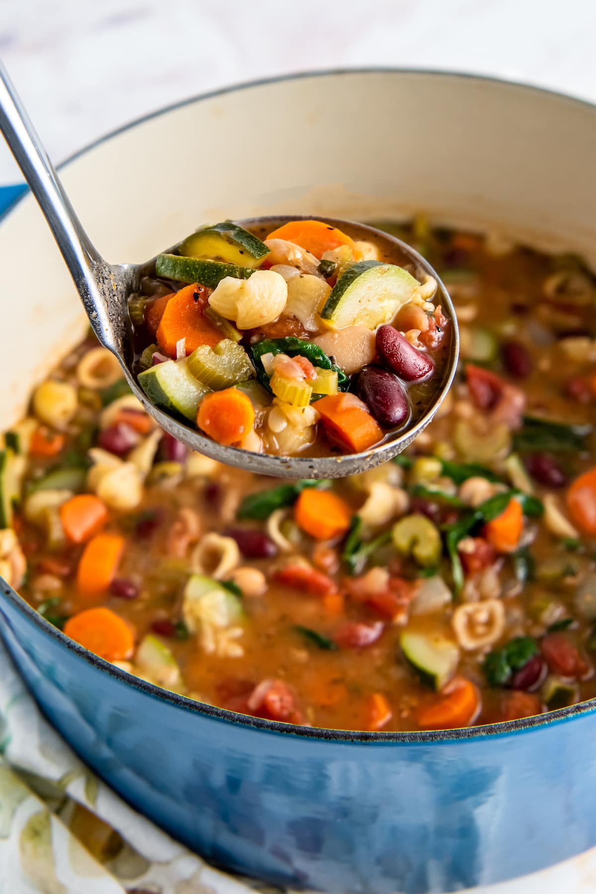 a ladle of soup with a lot of vegetables like carrots and zucchini