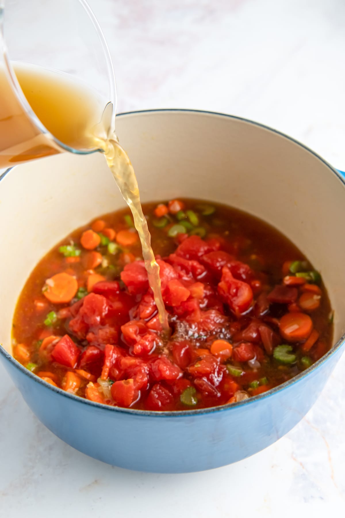 adding broth to a large pot with soup ingredients