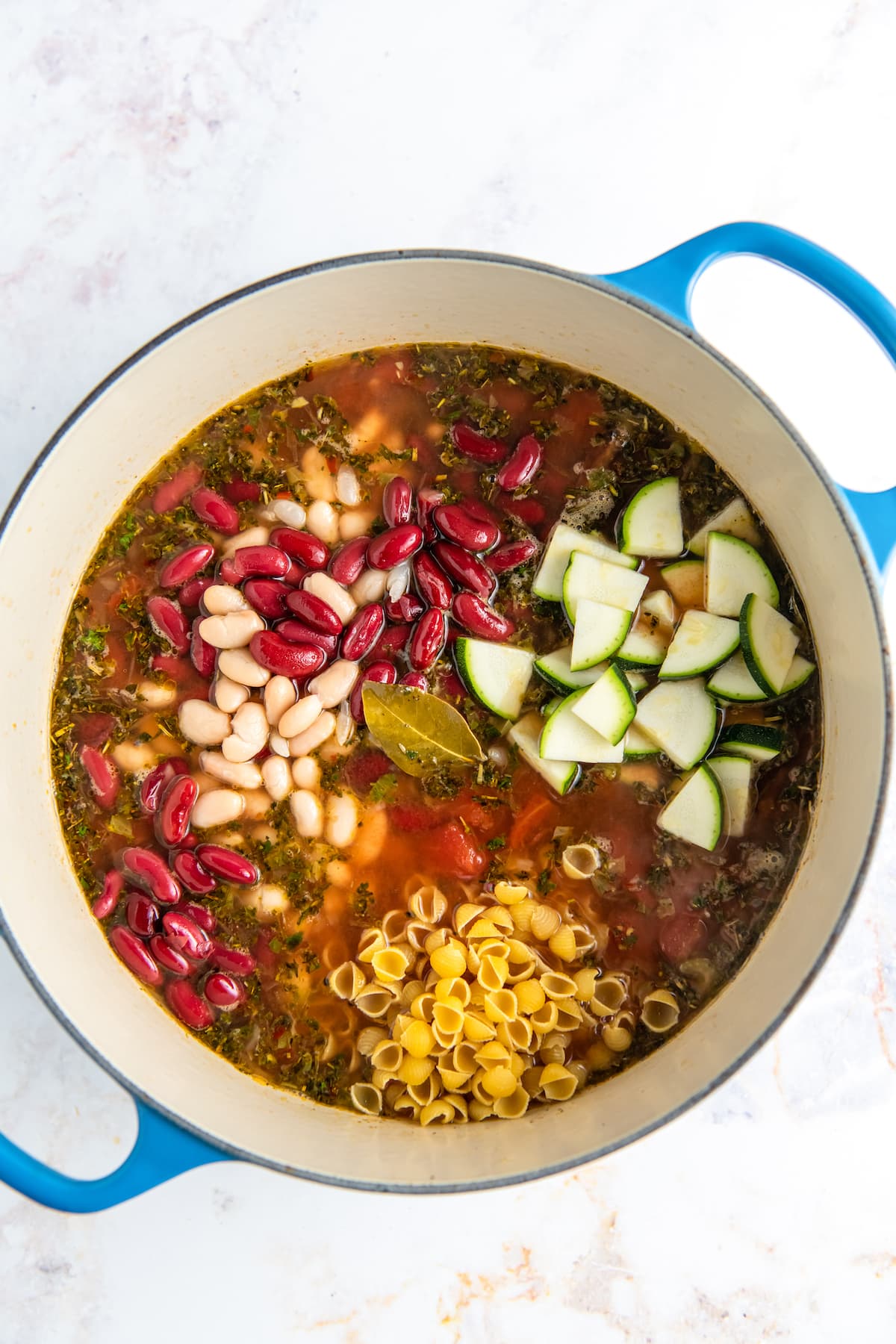 adding beans, zucchini, and noodles to a soup in a large pot