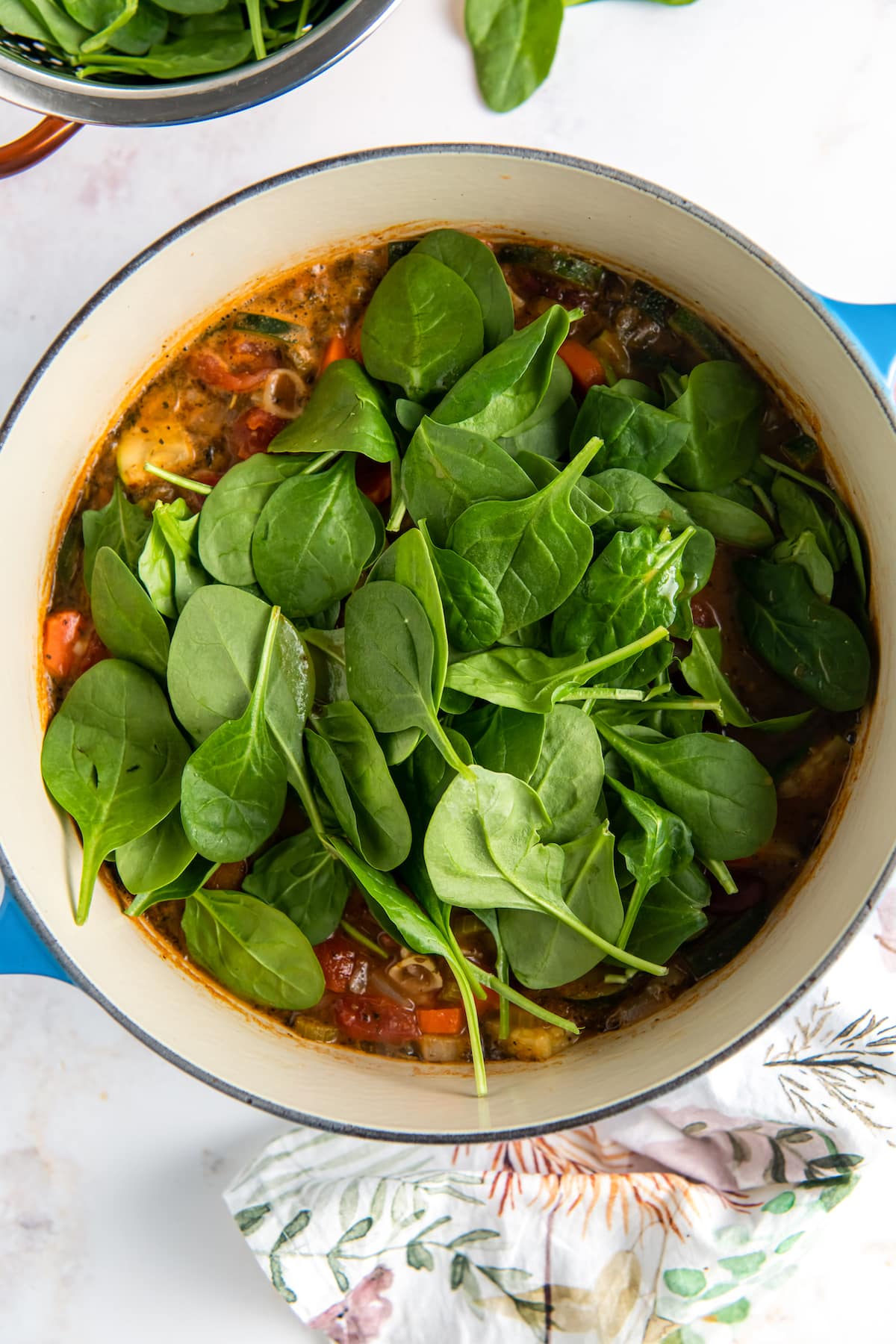 adding spinach to a large pot with soup