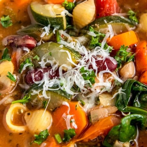 a bowl of minestrone soup with a rich tomato broth, vegetables, noodles, and cheese