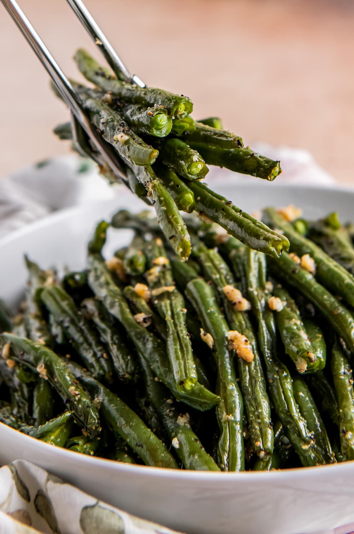 tongs grabbing a serving of roasted green beans out of a bowl