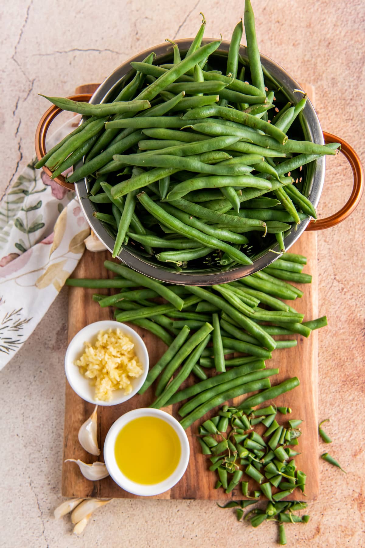 green beans on a cutting board with garlic and olive oil in small bowls on the side