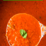 A ladle scooping up a serving of tomato basil soup out of a pot of tomato soup.