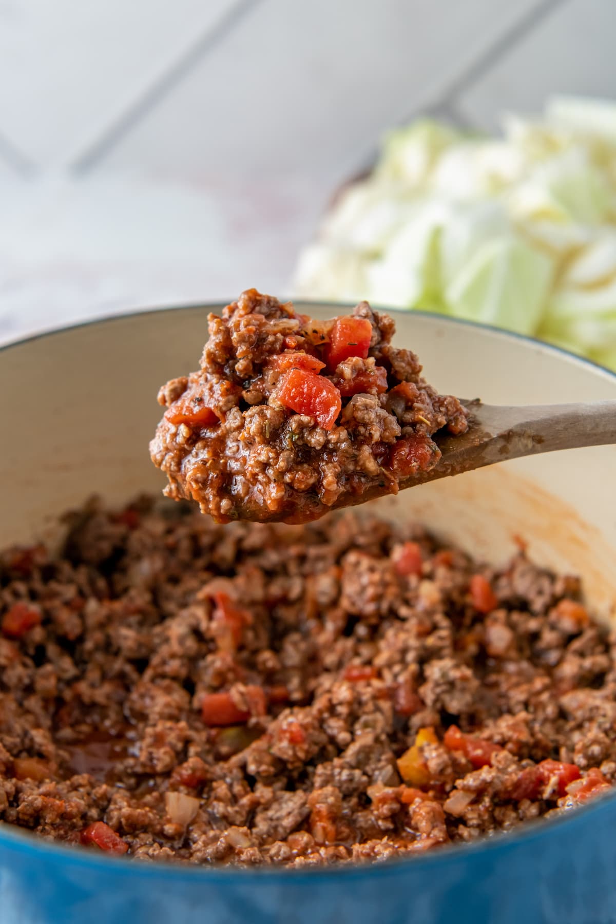 a scoop of ground beef and tomatoes over a large pot