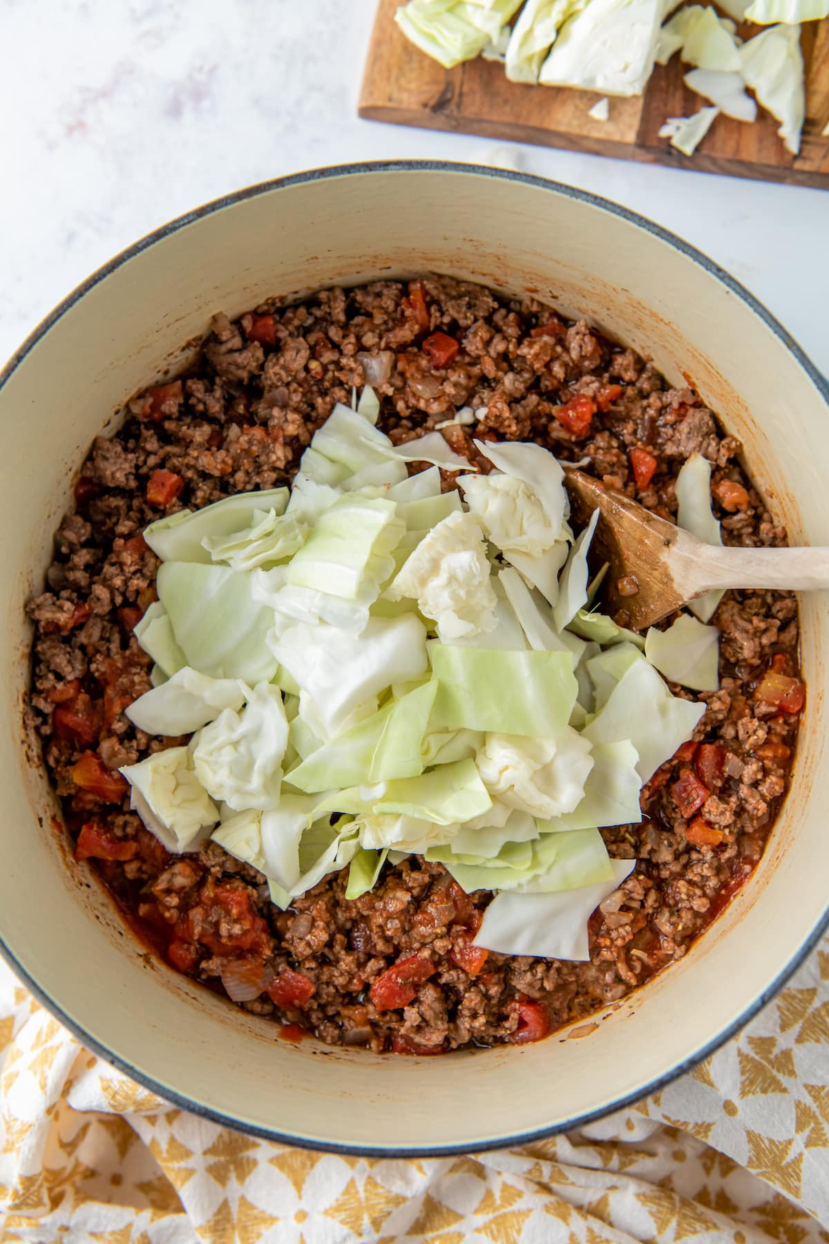 adding chopped cabbage to a pot of ground beef and tomatoes