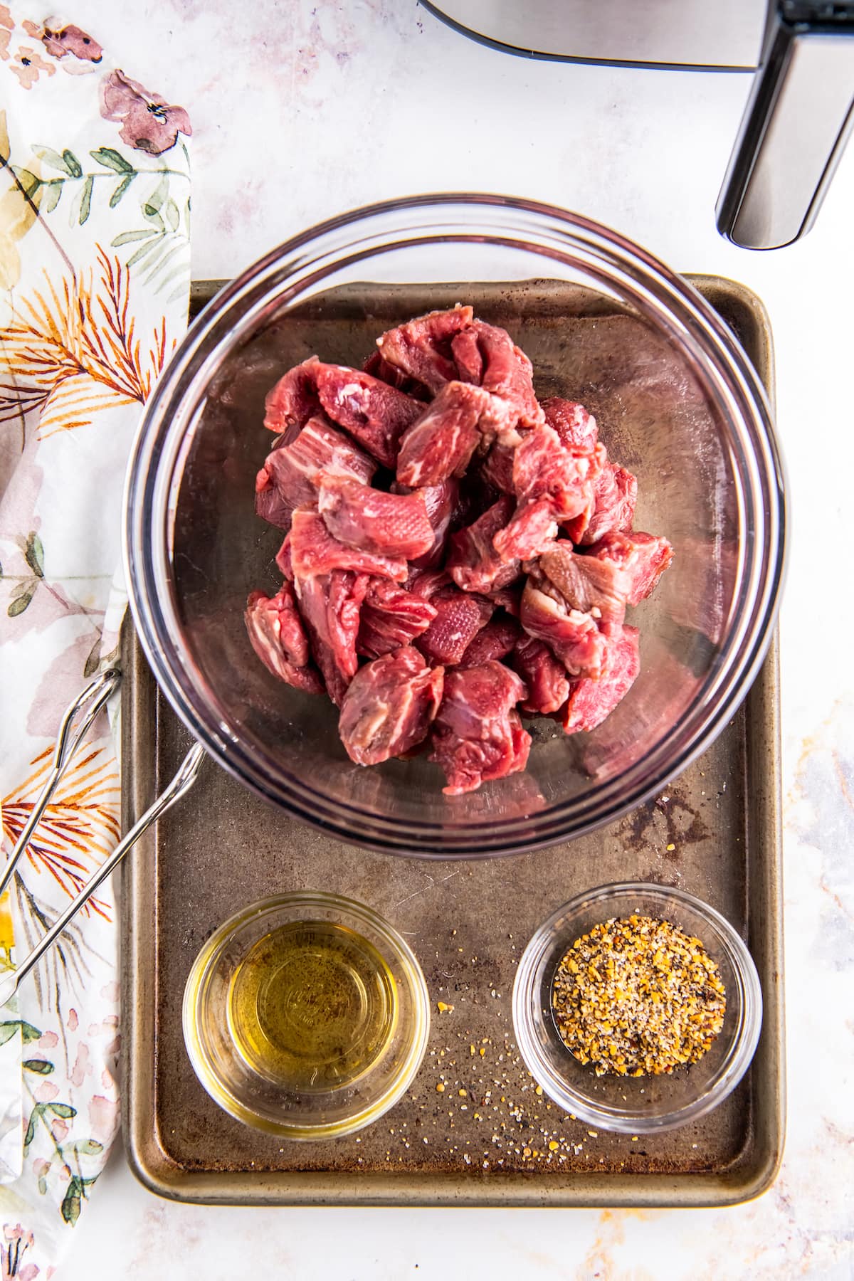 ingredients to make air fryer steak bites including cut up pieces of meat, oil, and seasoning