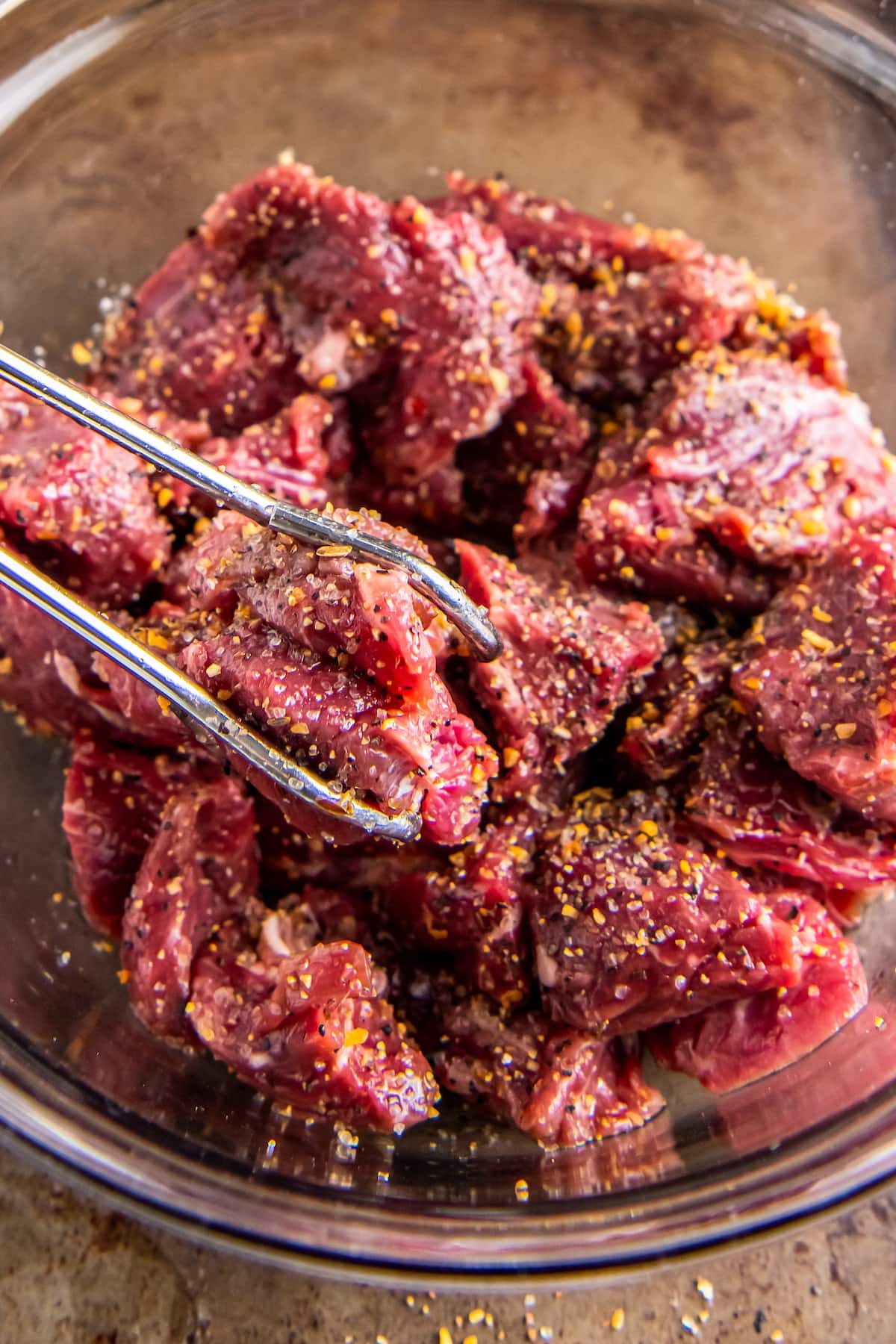 tossing pieces of beef with steak seasoning and using tongs