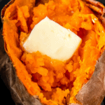 A sweet potato in an air fryer basket with a pad of butter.