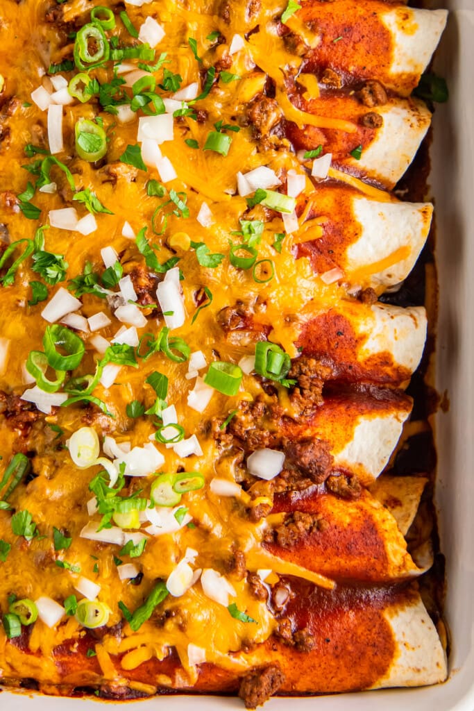 beef enchiladas that are topped with melted cheese, scallions, and diced onions