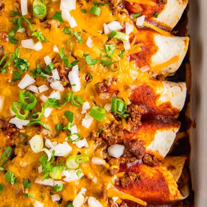 beef enchiladas that are topped with melted cheese, scallions, and diced onions