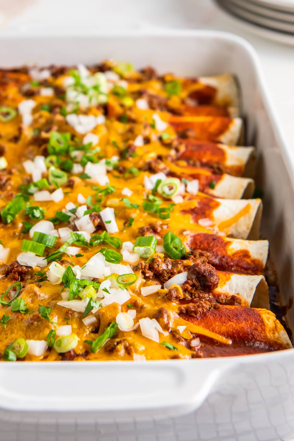 beef enchiladas that are topped with melted cheese, scallions, and diced onions