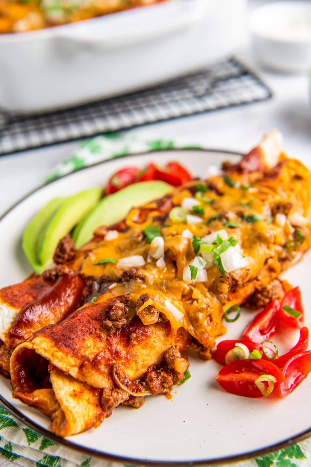 a plate of two rolled tortillas with red sauce and cheese on top with a side of avocado