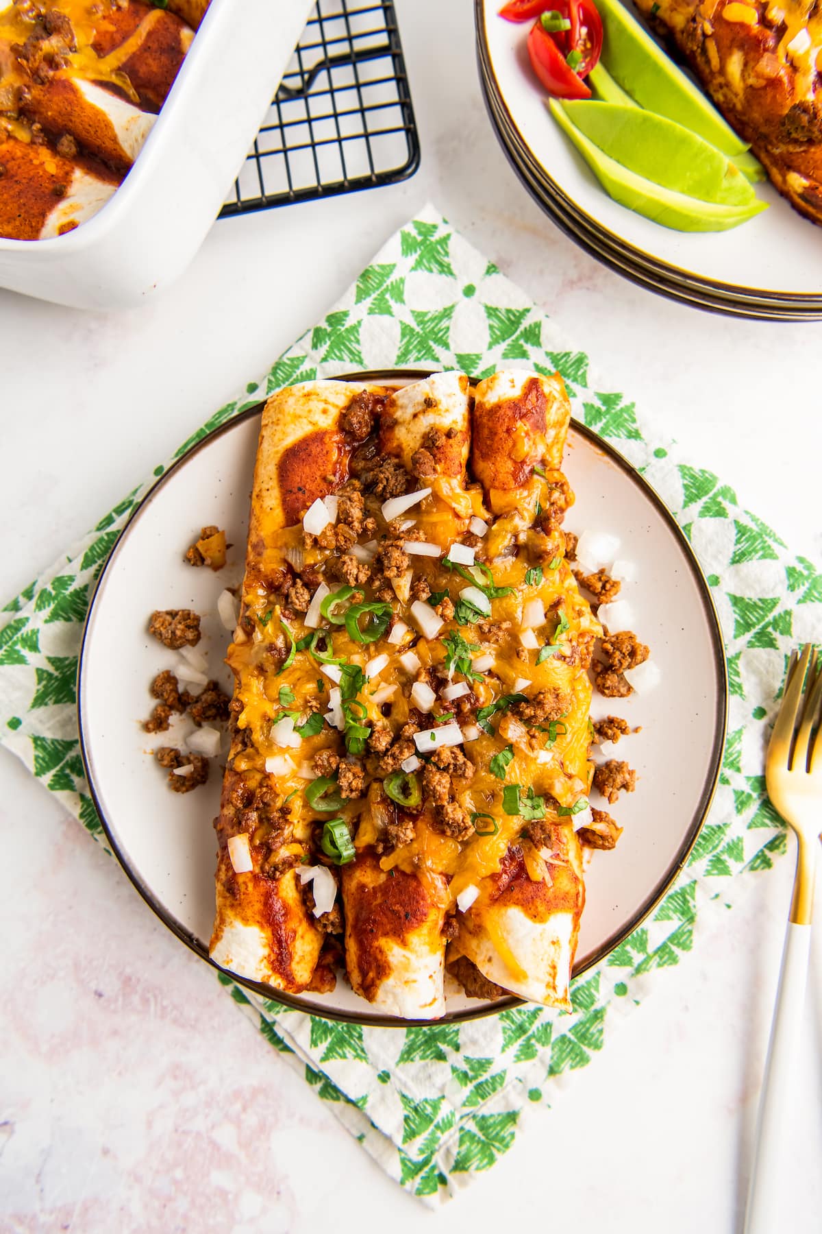 a plate with three enchiladas topped with red sauce, melted cheese, and diced onions