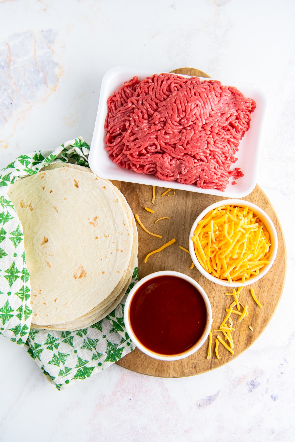 a round cutting board with tortillas, red sauce, ground beef, and cheese