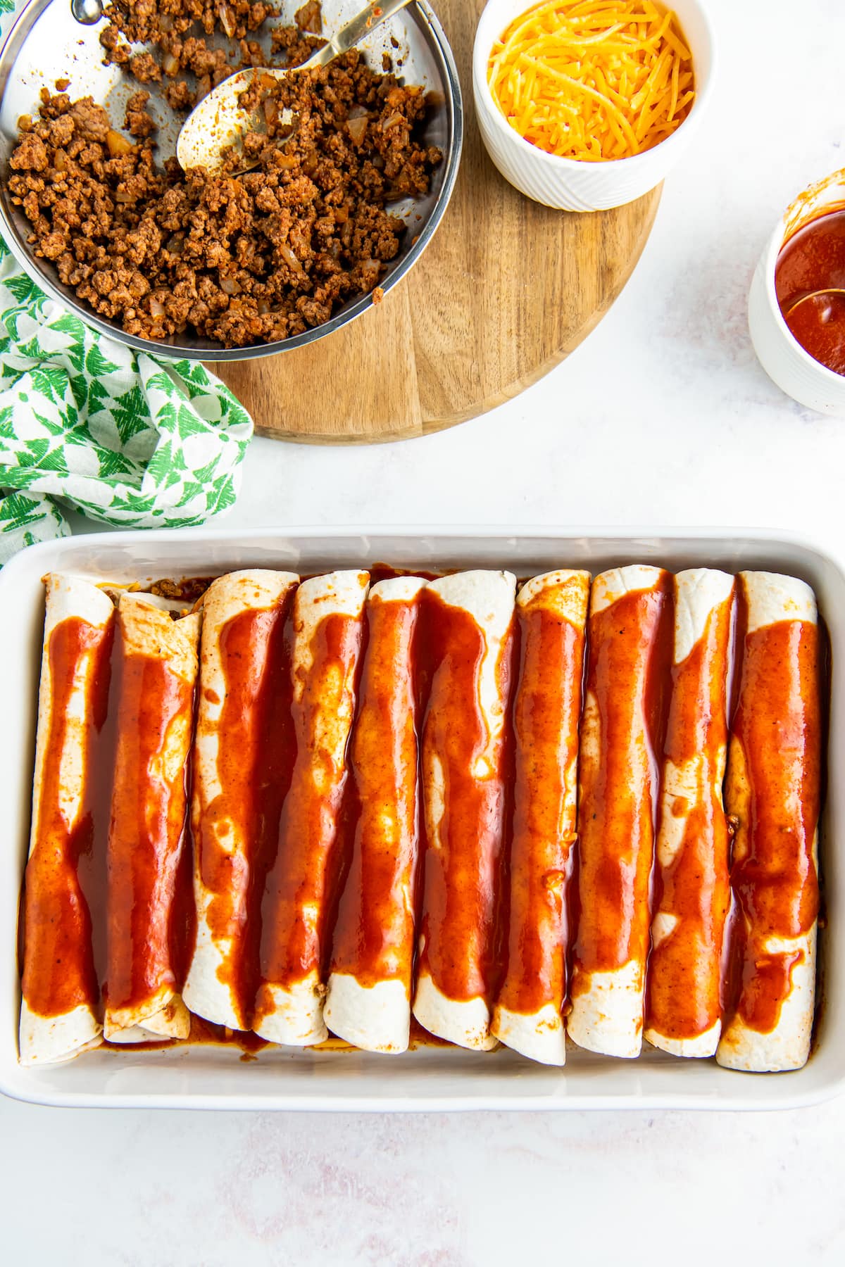 a casserole dish with rolled tortillas and red sauce poured on top