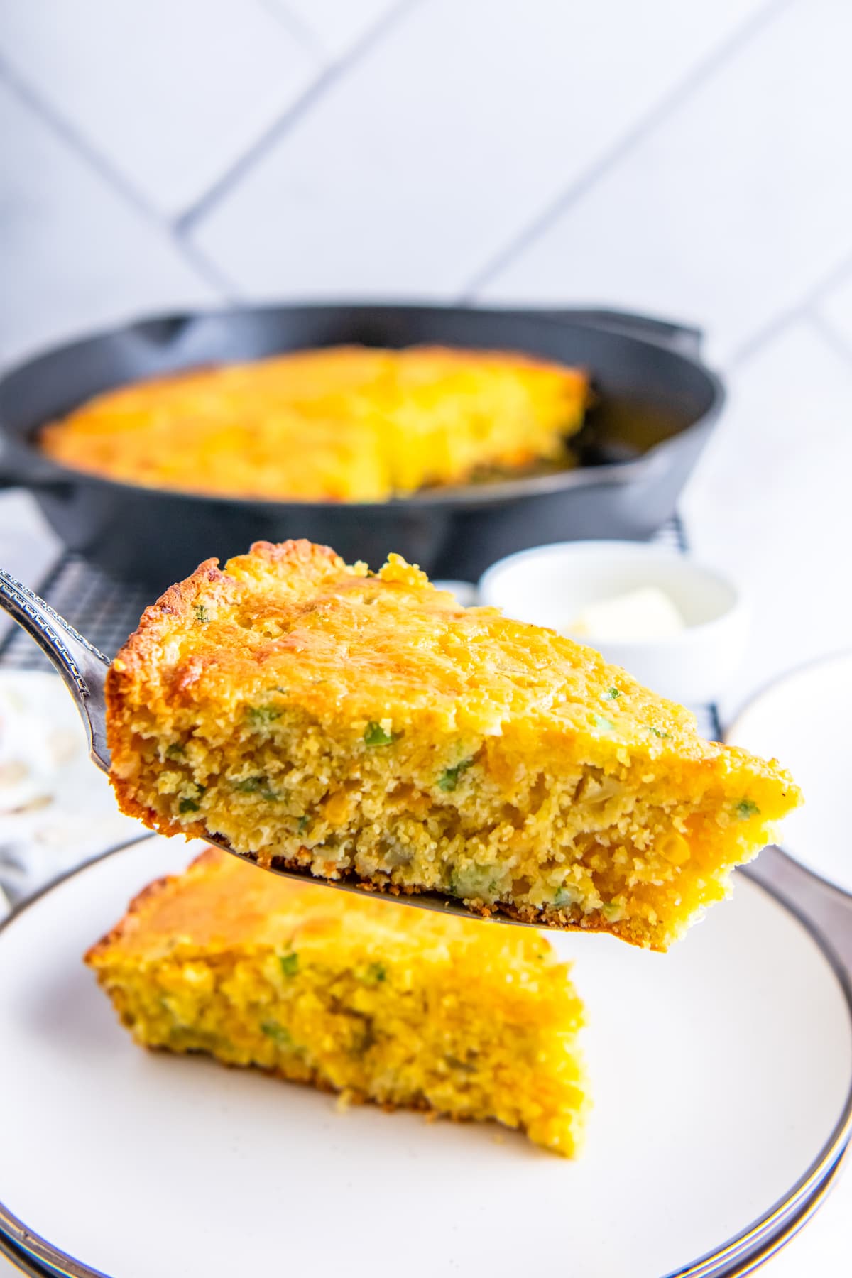 stacked sliced cornbread on a white plate with a skillet in the background