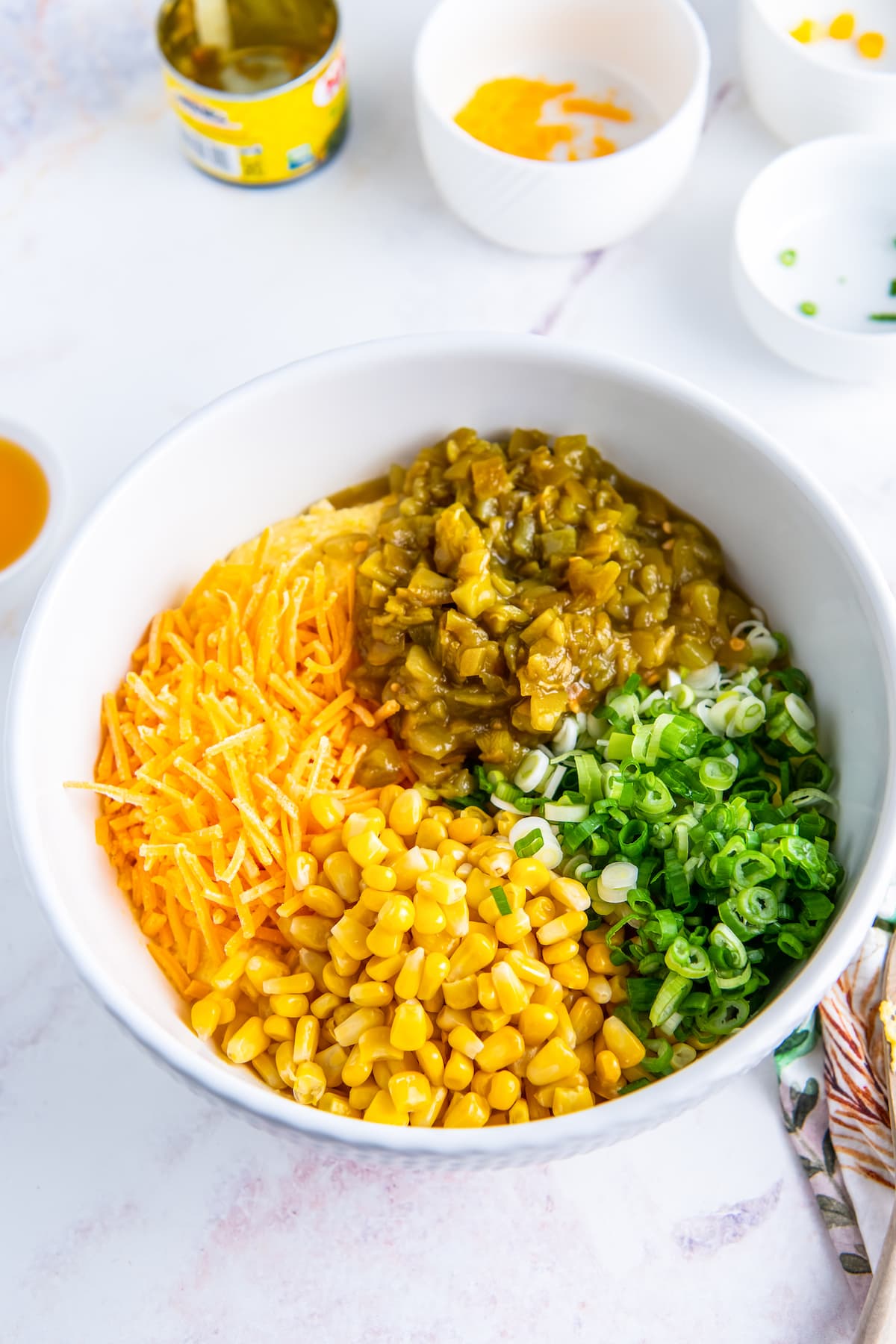 a bowl with shredded cheese, corn, scallions, and diced green chilis