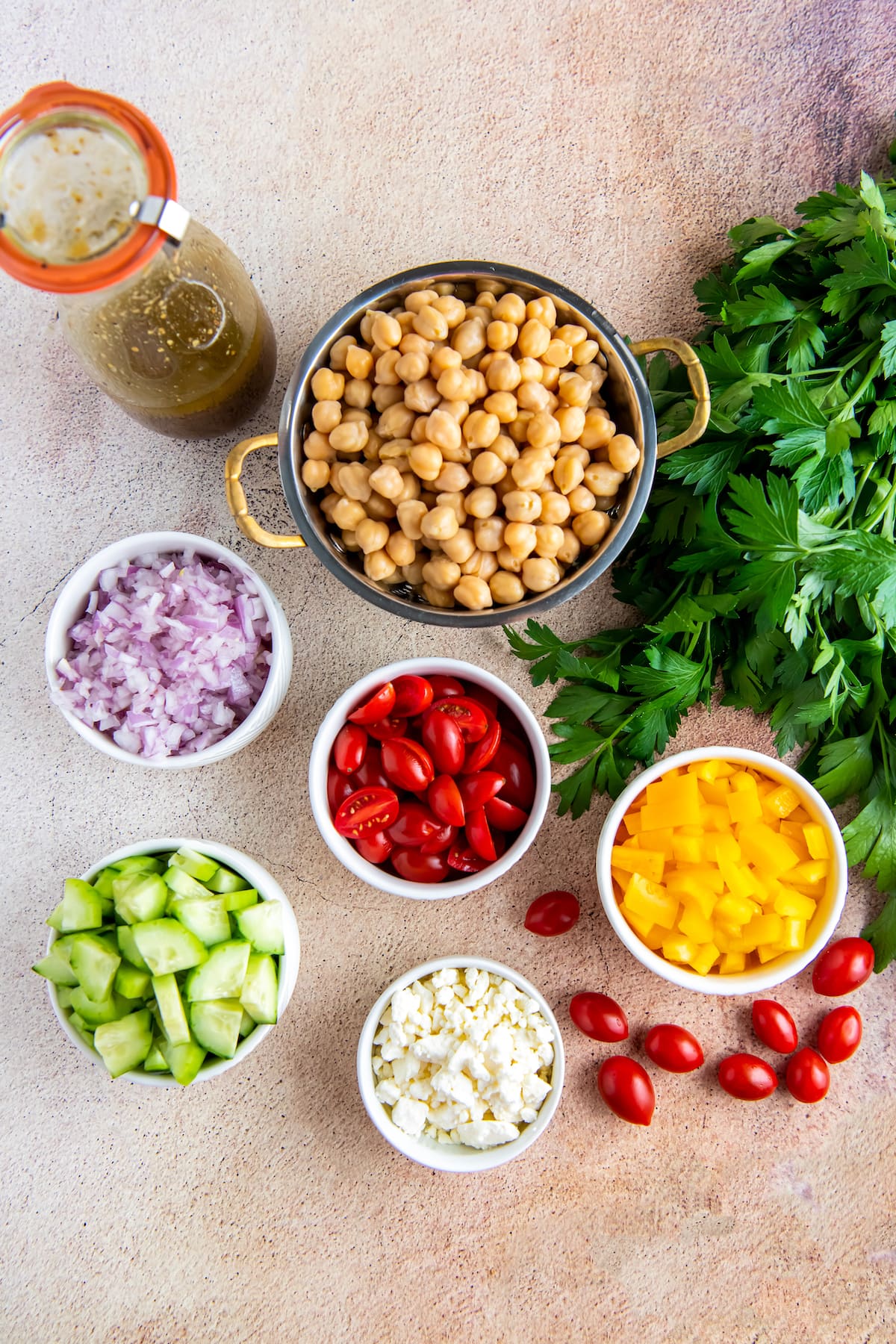 an assortment of ingredients in small bowls to make a chickpea salad like chickpeas, tomatoes, red onions, cucumbers, and fresh herbs