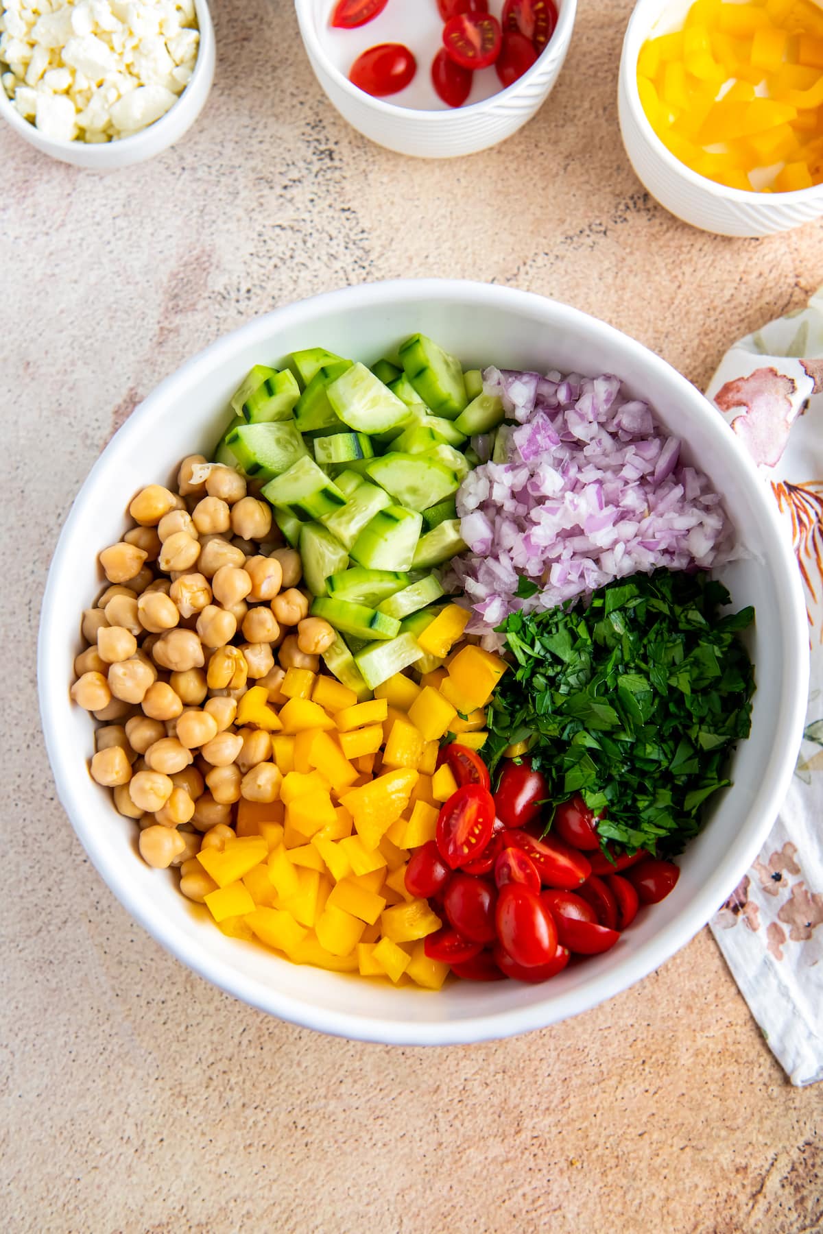 a bowl with divided ingredients including chickpeas, herbs, cucumbers, tomatoes, and yellow peppers