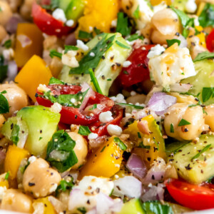 close up of a salad made with chickpeas, feta, cucumbers, herbs, tomatoes, and red onions