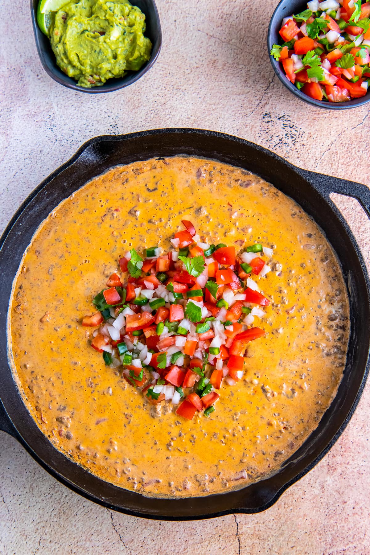 chili con queso in a cast iron skillet with garnishes of chopped tomatoes, peppers, and onions
